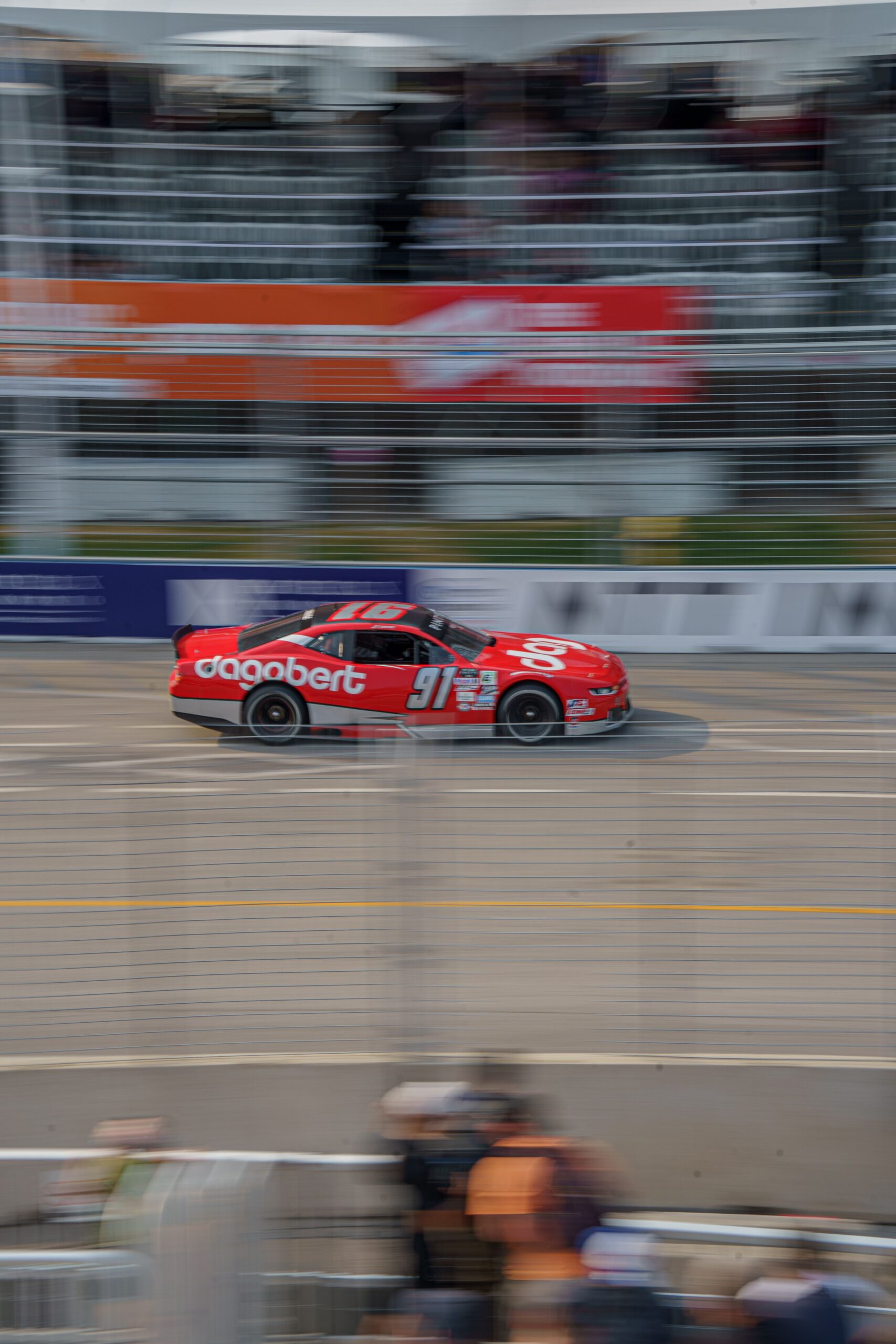 Dynamic image of a red race car speeding on a Toronto circuit during daytime, showcasing urban racing excitement.