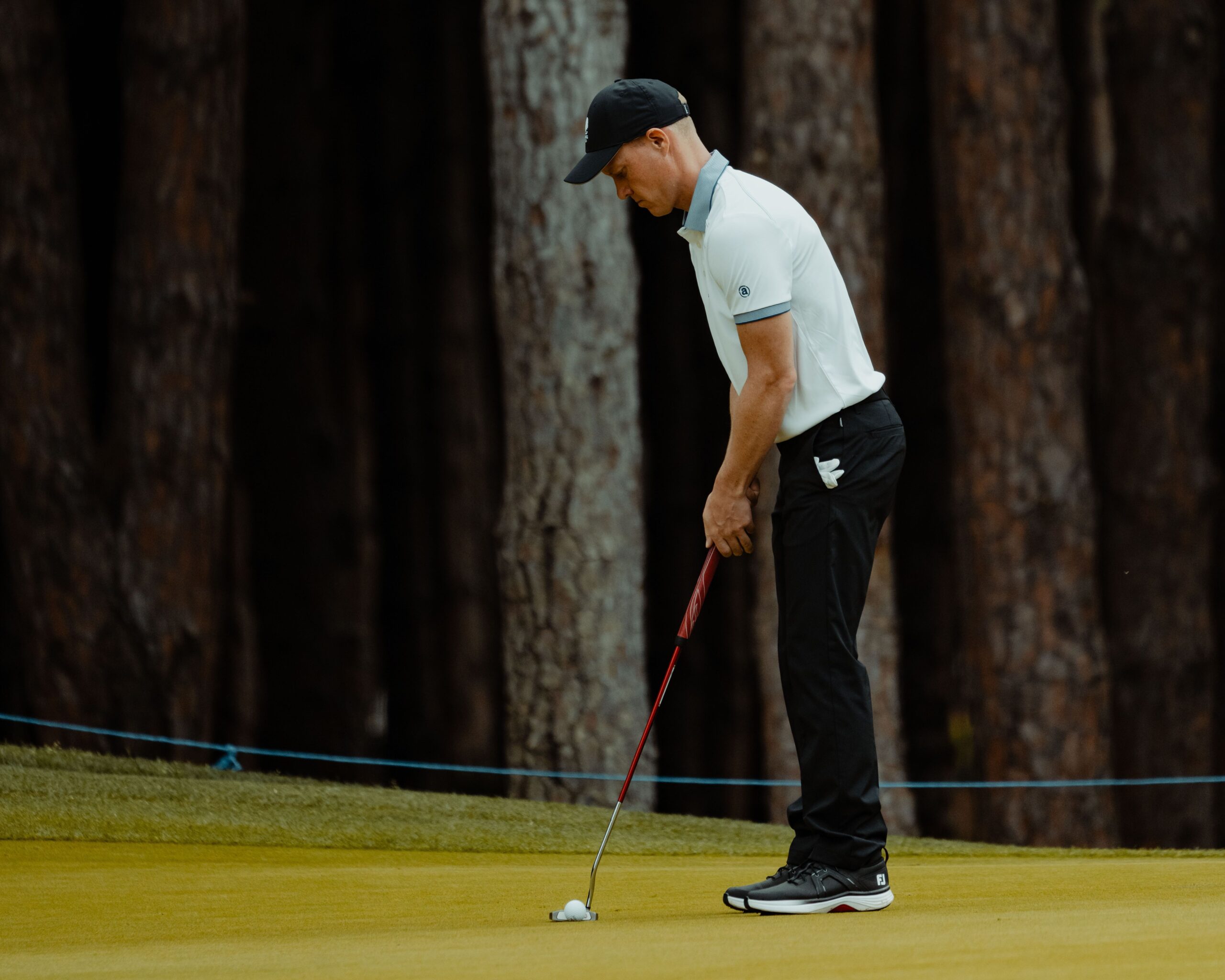 A golfer focusing on a putt on a serene Turkish golf course surrounded by trees.